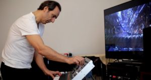 A man playing a MatrixBrute keyboard in front of a tv.